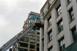 Worker in cherry picket against tall grey building