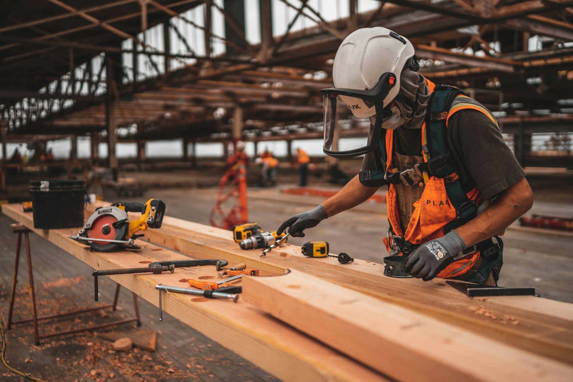 Man in PPE drilling long planks of wood on a workbench
